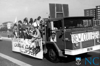 Black and white photograph - College residents riding a large flatbed truck with a banner 