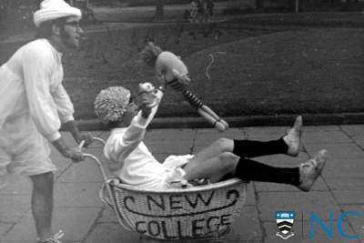 Photograph of college resident being pushed in a baby pram with New College emblazoned on the side